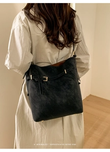 Black matte leather bucket bag with gold buckle detail shown on a beige trench coat