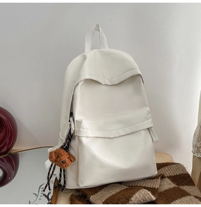 Detail of a creamy white large capacity backpack with a cute brown plush bear pendant