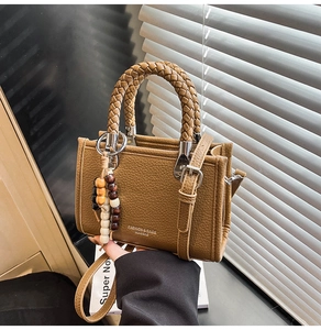 Detailansicht der braunen Tasche aus Narbenleder mit Flechtgriff und Perlenanhänger