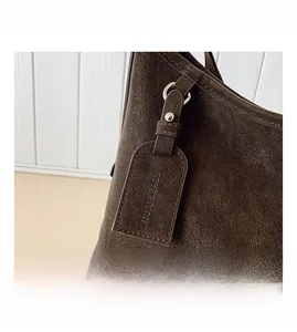 Close-up of a brown leather tote bag detail with logo-embossed tag and gold-tone rivets