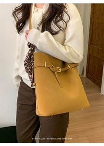 Model wearing a mustard leather bucket bag decorated with a brown printed scarf