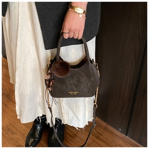Détail du sac seau marron foncé avec logo doré, pompon en fourrure et gland perlé
