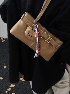 Vintage khaki underarm bag with decorative buckles and plush bear charm on a model