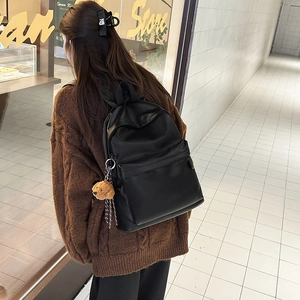 Rear view of a black leather backpack with a plush bear charm worn by a model