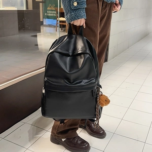 Close-up of black PU leather backpack featuring a side pocket and brown teddy bear charm