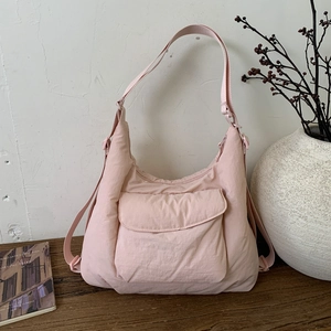 Detail of light pink nylon crescent crossbody bag with flap pocket on a wooden surface