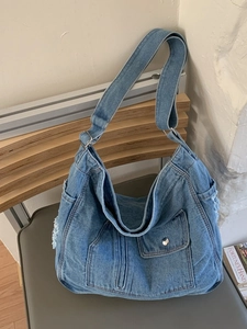 Large blue washed denim shoulder bag with fringe details and front pockets for daily commute