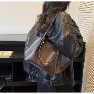 Détail d'un grand sac cabas vintage en similicuir marron brillant porté à l'épaule du modèle
