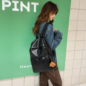 Detail of a black faux leather backpack with a cute brown plush dog charm accessory