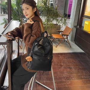 Close-up of a minimalist black leather backpack featuring a cute brown teddy bear charm