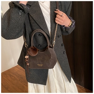 Borsa a secchiello marrone scuro con catena dorata e pompon indossata con cappotto