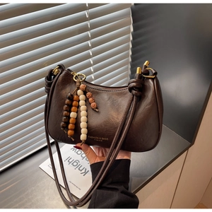 Détail du sac sous l'aisselle en cuir marron foncé avec charm décoratif en perles de bois