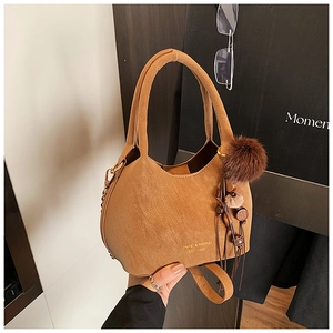 Détail du sac seau marron en PU avec logo doré, poignée cylindrique et pompon en peluche