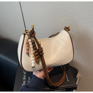 Detail view of cream leather dumpling bag with contrast piping and retro bead charm