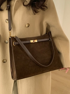Grand sac cabas en daim marron avec boucle dorée porté par un mannequin sur un manteau