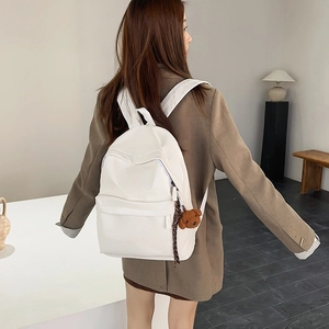 Detailed side view of a white minimalist backpack featuring a plush bear charm accessory