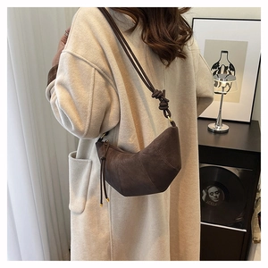 Detail of a dark brown suede crescent bag featuring knot shoulder strap and gold zipper