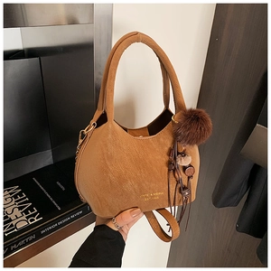 Détail d'un sac seau marron avec logo doré, breloque à pompon et accessoire boule peluche