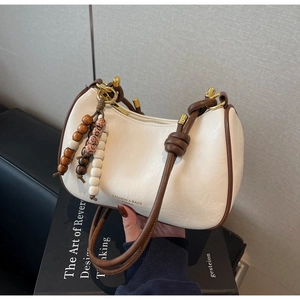 Détail du sac crème avec bandoulière en corde marron et pendentif perlé sur livres