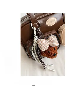 Gros plan du sac en cuir verni marron avec pendentif ours en peluche et nœud à carreaux