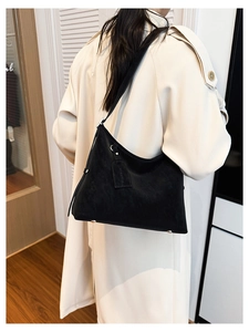 Detail of black matte leather tote bag with branded tag on classic beige trench coat