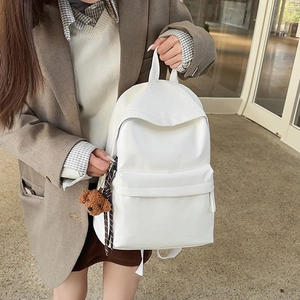 Detailed view of a white travel backpack with a brown teddy bear keychain on a model