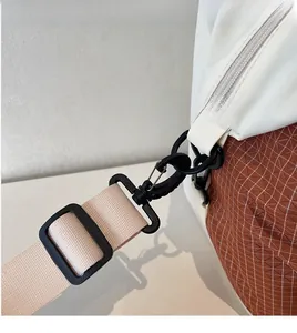 Detail of adjustable beige woven strap with black clips on a brown plaid shoulder bag