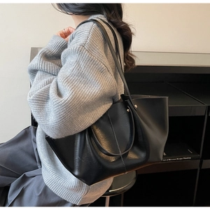 Sac fourre-tout noir minimaliste en similicuir porté à l'épaule avec un pull en maille
