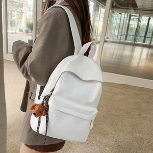 Detailed view of white minimalist backpack featuring a cute brown plush bear keychain charm