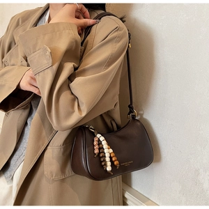 Détail du sac croissant en cuir marron foncé avec perles sur un trench-coat kaki