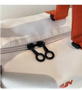 Detail of double-way circular ring zippers on off-white nylon bag with orange straps