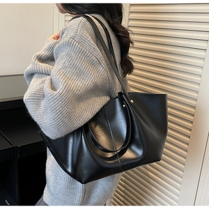 Détail du cabas en cuir noir brillant montrant la texture lisse et la couture latérale