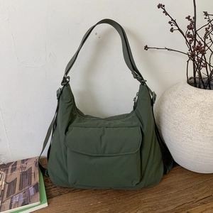 Close-up of olive green pleated nylon shoulder bag with adjustable strap on wooden table