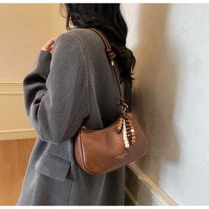 Detail view of a vintage brown leather crescent bag with wooden bead charm on shoulder