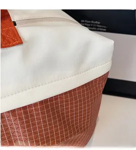 Detail view of large shoulder bag featuring white textured fabric and orange grid pattern