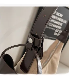 Detail of silver cylindrical metal buckle on beige fabric bag with brown leather strap