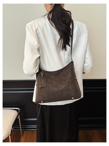 Model wearing a large dark brown suede hobo tote bag with minimalist shoulder strap style