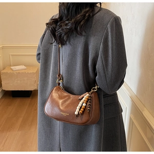 Détail d'un sac bandoulière demi-lune marron avec pompon en perles et lettrage doré
