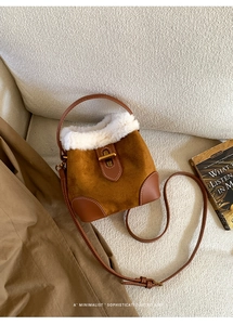 Detail of vintage brown suede bucket bag with white shearling trim on a white sofa