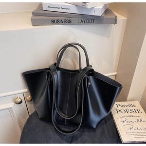 Détail d'un sac cabas noir minimaliste avec doubles poignées sur une surface bleue