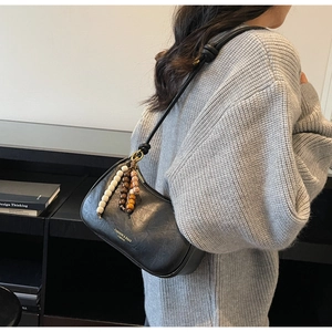 Détail d'un sac demi-lune noir avec pompon en perles de bois et bandoulière à nœuds