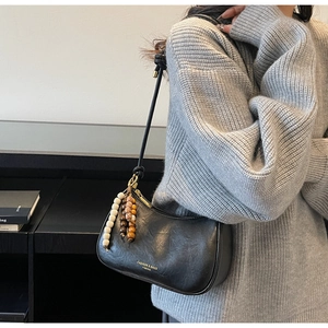 Détail du sac demi-lune noir avec pompon en perles bohème et logo doré sur le cuir