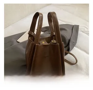 Detailansicht einer braunen Leder-Tote-Bag mit Logoprägung auf einem grauen Sakko