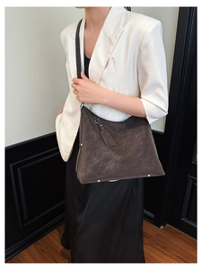 Detail of a large dark brown matte tote bag showing side metal zippers and rivets