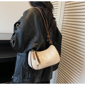 Détail d'un sac sous le bras crème avec liseré marron et pendentif en perles de bois