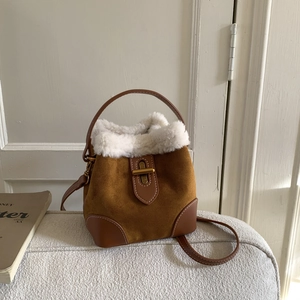 Detail of brown suede bucket bag with white faux shearling trim and bronze buckle