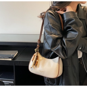 Détail du sac sous le bras crème avec bordure brune et breloque à pompon en perles de bois