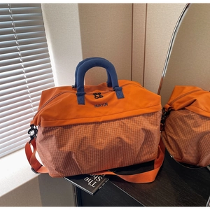 Detail of large travel tote with orange plaid pattern and blue cylindrical top handles