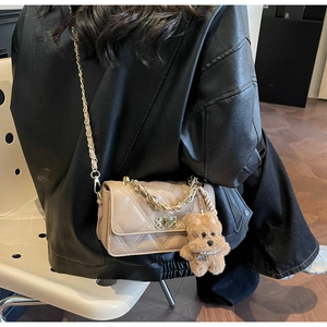 Close-up of apricot quilted crossbody bag with gold chain and plush bear charm detail