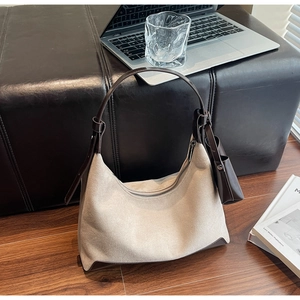 Detail of beige suede crescent tote bag with brown leather trim in a workspace setting